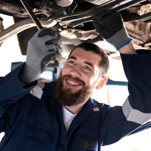 Lachender KFZ-Techniker bei der Arbeit unter einem Fahrzeug
